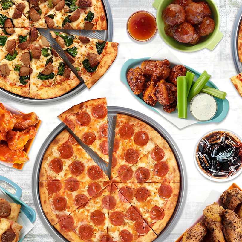 Two pizzas, wings, meatballs, and a drink on a white wooden table at Guido's Pizza & Pasta.