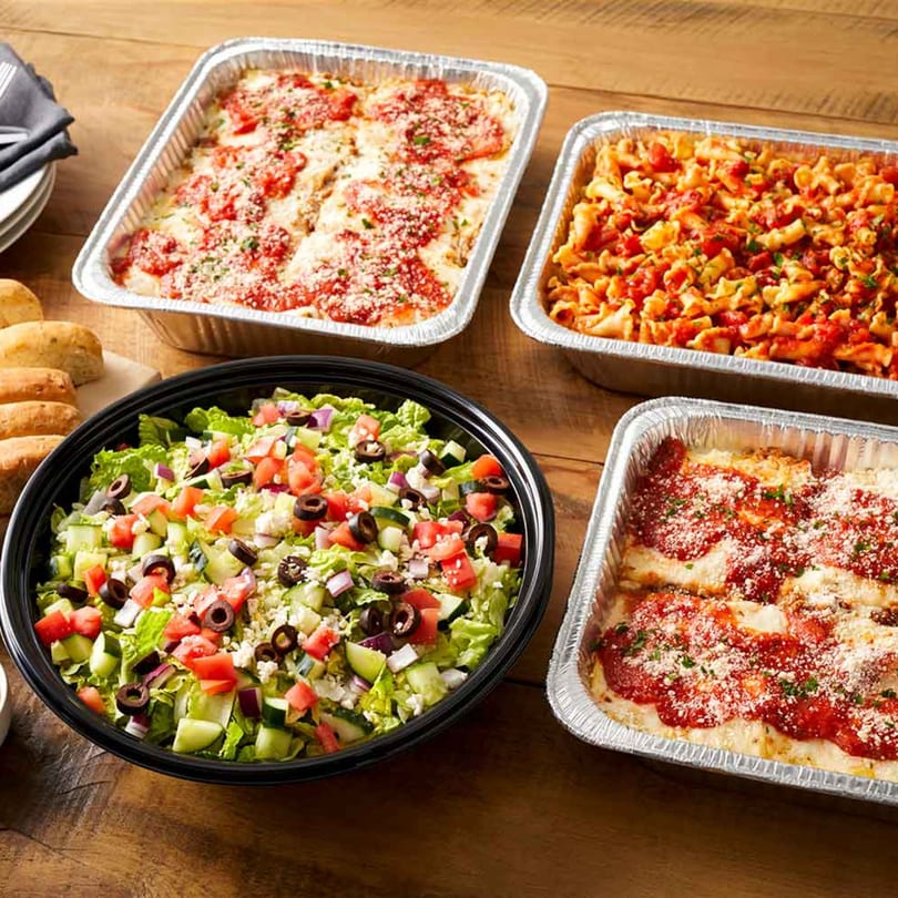 Guido's Pizza & Pasta catering spread with lasagna, pasta, salad, and bread rolls.